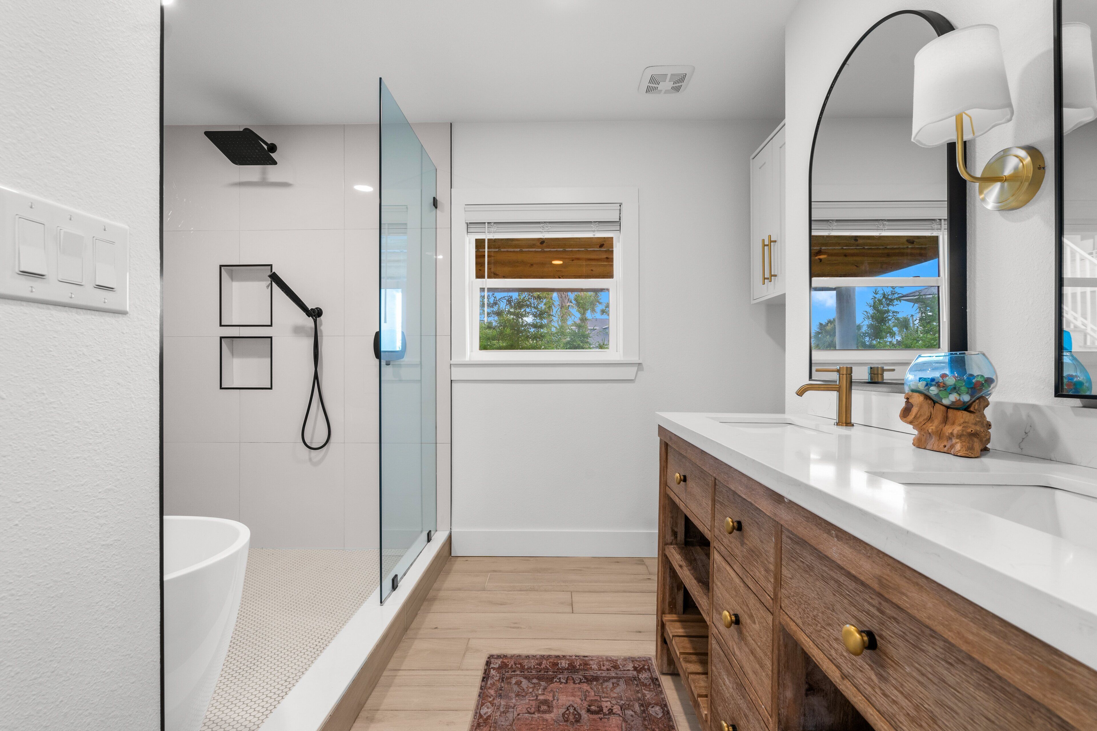 Ein modernes Badezimmer mit Duschkabine aus Glas, Waschbecken in Weiß, Holz-Badmöbel und einem Fenster mit Jalousien.
