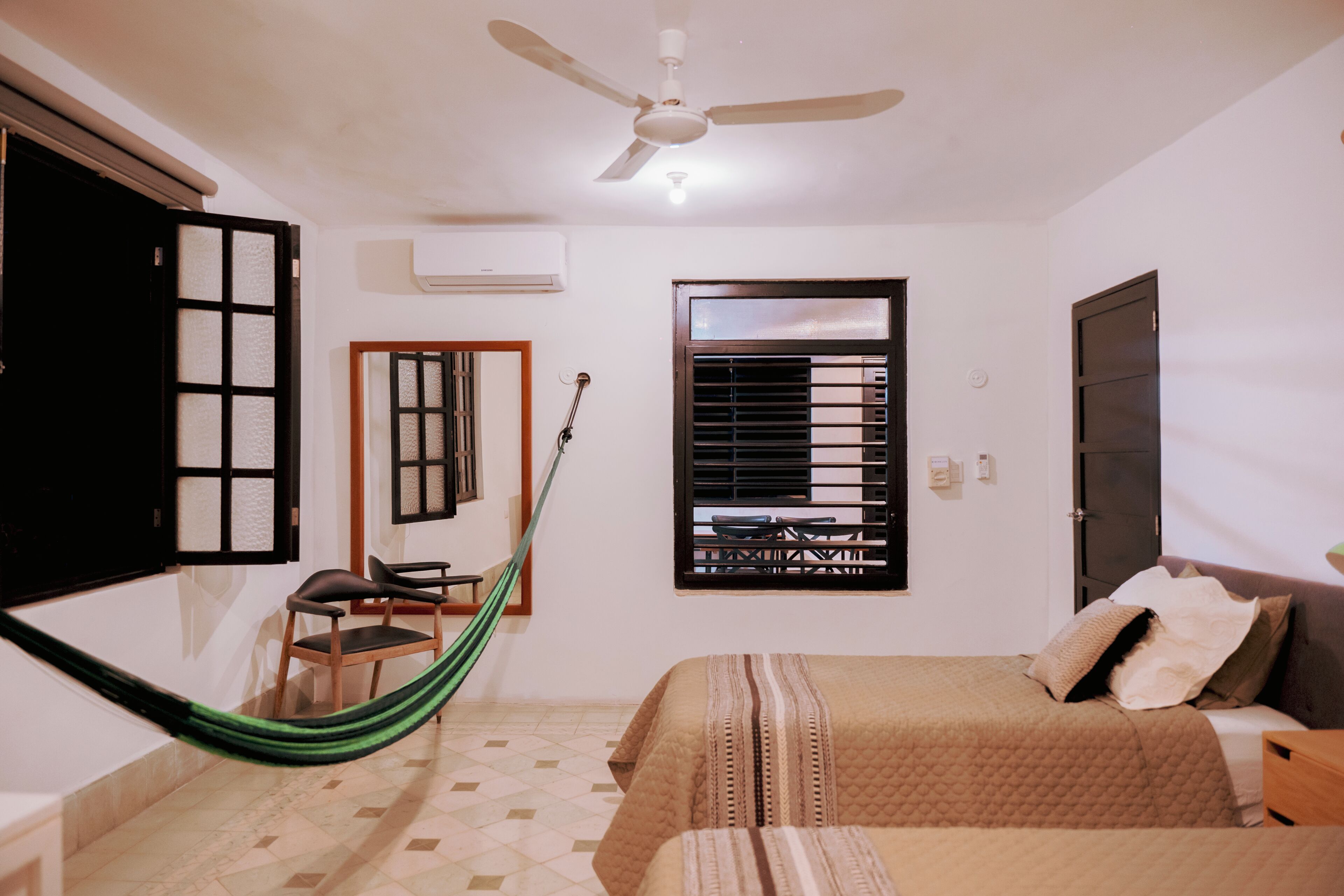 A bedroom with a bed, a chair, a hammock, a ceiling fan, and a window with blinds.