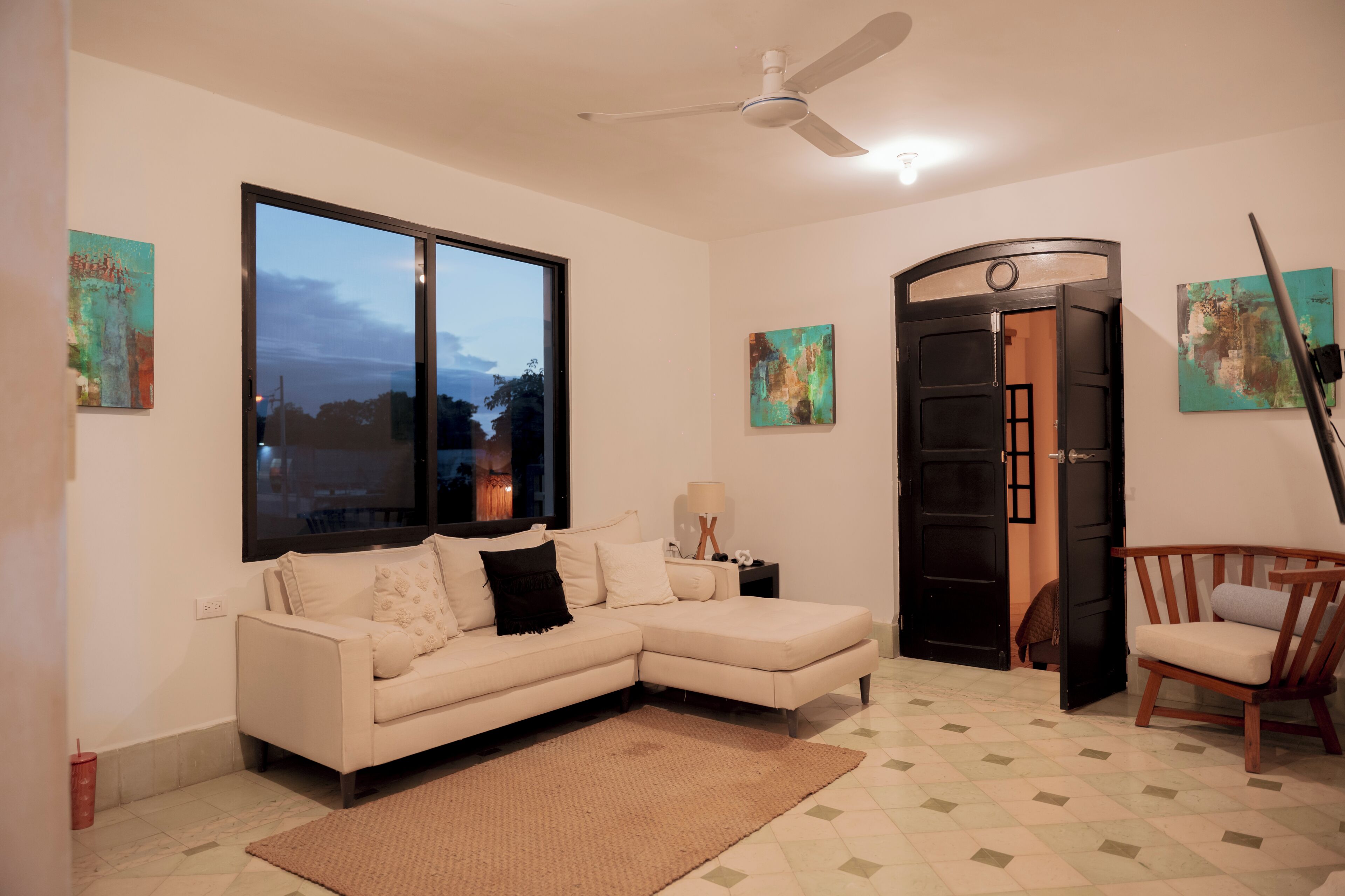 A living room with a sofa, a coffee table, a chair, a ceiling fan, and artwork on the walls.