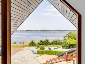 Blick durch ein dreieckiges Fenster auf einen See mit einer Sandküste und grünen Bänken.