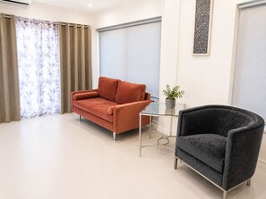 Ein modernes Wohnzimmer mit einer Couch, einem Sessel, einem Glastisch und einer Zimmerpflanze.