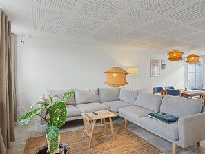 Una sala de estar moderna con un sofá seccional gris, una mesita de madera, una planta verde grande y dos lámparas colgantes de mimbre.