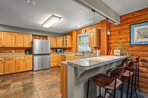 Eine Küche mit Holzausstattung, einem Kühlschrank, einer Mikrowelle, einer Spüle und einer Bar mit Hockern.