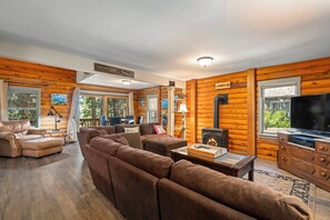 L’intérieur d’une cabane en rondins, avec un grand canapé, une cheminée, un téléviseur et un plafond en bois.