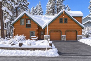 A log cabin with a garage and a front porch, surrounded by snow-covered trees. - 920 Dorcey | 5BR/4BA Incline Village Retreat w/ Game Room (Incline Village)