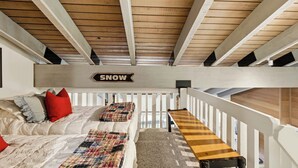 Une chambre de style « loft » avec un plafond en pente, un lit avec une couette à carreaux, un banc et un panneau décoratif portant l’inscription « NEIGE ».