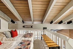 Ein Schlafzimmer im Loft-Stil mit schrägverdeckter Decke, einem Bett mit Karomustern, einer Bank und einem Schild mit der Aufschrift 'SNOW'.