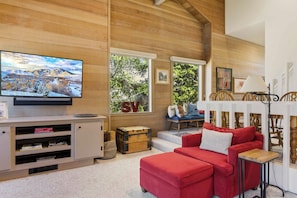 Ein Wohnzimmer mit Fernseher, einem roten Sofa, einem Fernsehschrank aus Holz und einer weißen Wand mit großem Fenster.