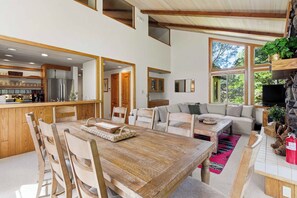 Un amplio salón con una mesa de comedor de madera, techos altos y ventanas grandes.
