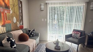 A living room with a sofa, armchair, coffee table, patterned rug, and a large abstract painting on the wall. - Braves Retreat 5 Min to Truist Park & The Battery (Smyrna)