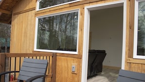 A wooden deck with two chairs, a door leading inside, and a window with a view of trees.