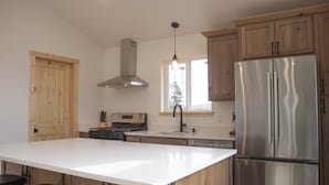 A modern kitchen with a large island, stainless steel appliances, wooden cabinets, and a window providing natural light.