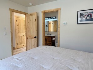 A bedroom with a bed, wooden wardrobe, a mirror, and a bathroom with a sink and toilet. - Welcome to Sky Ranch, a spacious, warm newly built home ready to welcome you. (Talkeetna)