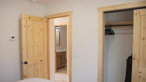 A bedroom with a wooden door, a closet with hanging clothes, and a bathroom visible through an open door.
