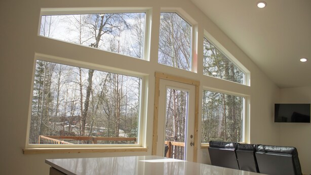 A kitchen with large windows, a dining area with chairs, and a TV mounted on the wall.