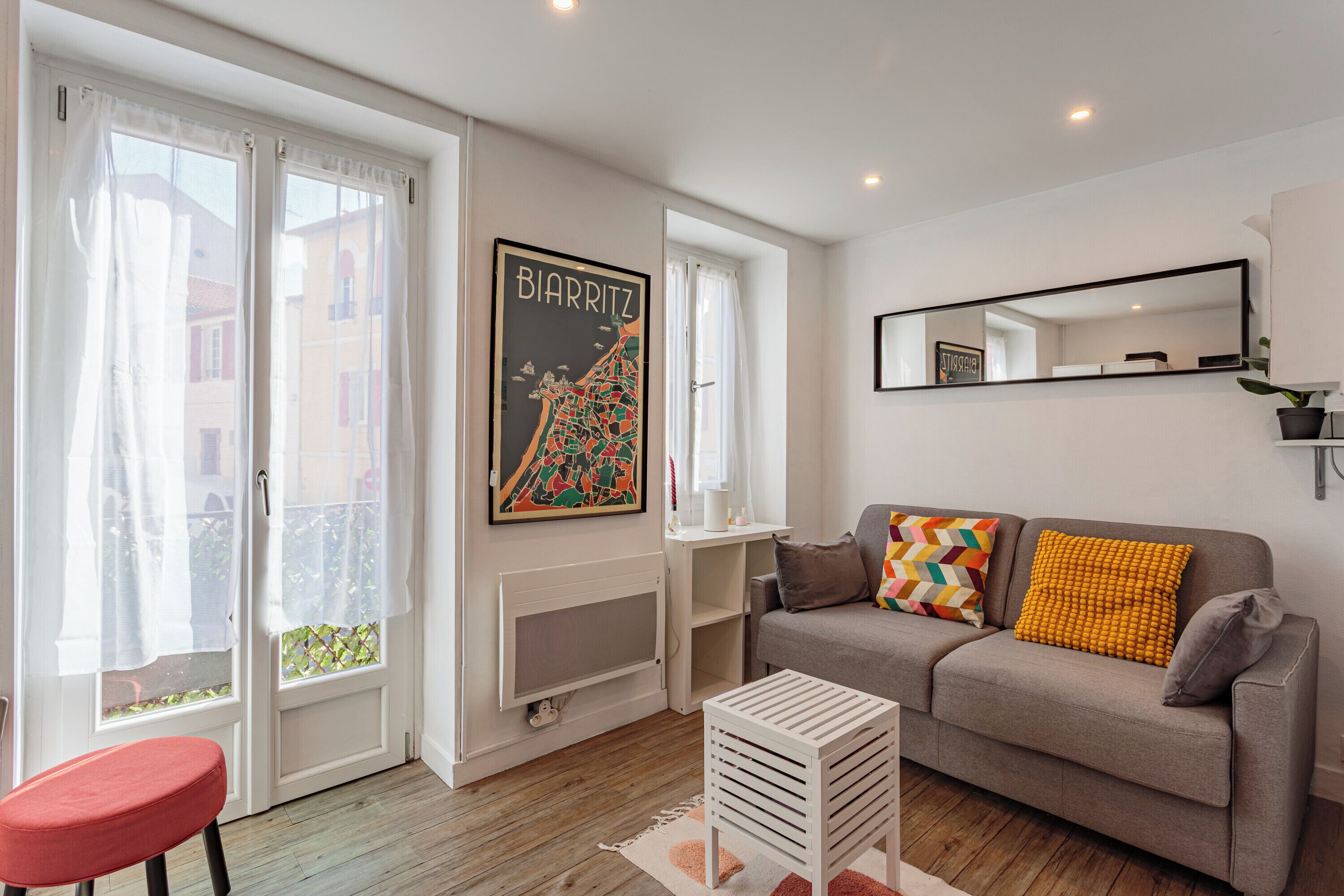 Een woonkamer met een bank, een rode stoel, een witte salontafel, een ingelijste kaart en een spiegel aan de muur.