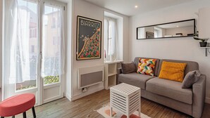 Una sala de estar con un sofá, un sillón rojo, una mesa de centro blanca, un mapa enmarcado y un espejo en la pared.