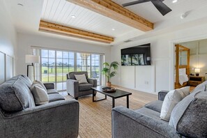 A spacious living room with a large window, grey sofas, a coffee table, and a ceiling fan. - Centre Court Pacifica Near Disney, Golf Course, WaterPark (Kissimmee)
