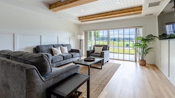 A spacious living room with a grey sofa set, a coffee table, and a large window offering a view of the outdoors. - Centre Court Pacifica Near Disney, Golf Course, WaterPark (Kissimmee)