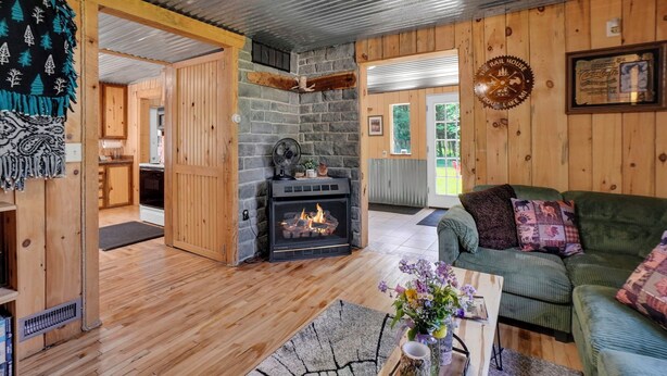 A cozy cabin interior with a fireplace, wooden walls, a green couch, and a dining area. - New Listing! 4 Bedroom Home 2 mins from the Lake-Boating-Fishing-Fire Pit (Trout Lake)