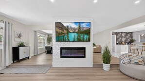 A modern living room with a fireplace, a mounted TV, and a dining area.