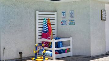 A poolside area with a white pool ladder, a children's play structure, and various pool accessories.