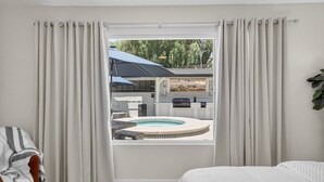 A bedroom with a window overlooking a pool and outdoor kitchen area.