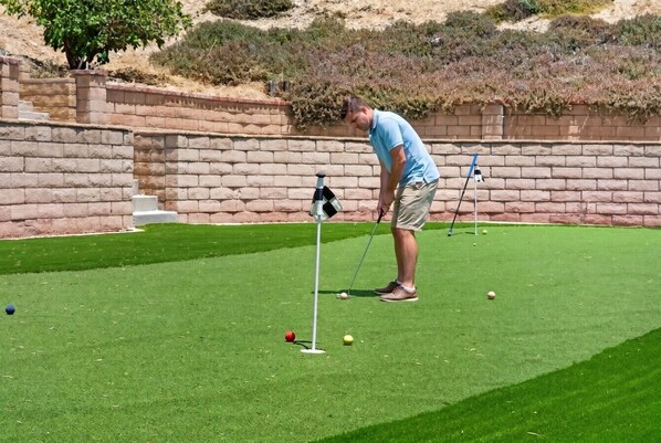 Una persona juega al golf en un campo verde con un muro de ladrillo al fondo.