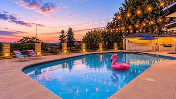 A swimming pool with a pink flamingo float, lounge chairs, and string lights.