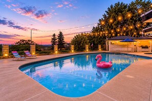 Una piscina con un flotador de flamenco rosa, sillas de descanso y luces colgantes.