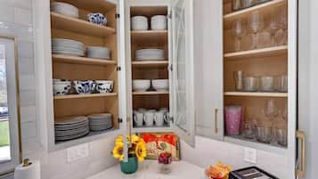 A kitchen with open cabinets displaying plates, bowls, and glasses. There is a vase with sunflowers on the counter.