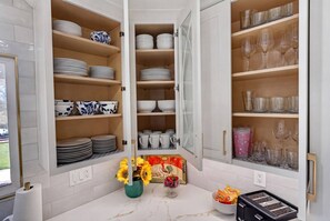 Cocina con armarios abiertos que exhiben platos, tazones y vasos. Hay un florero con girasoles en la encimera.