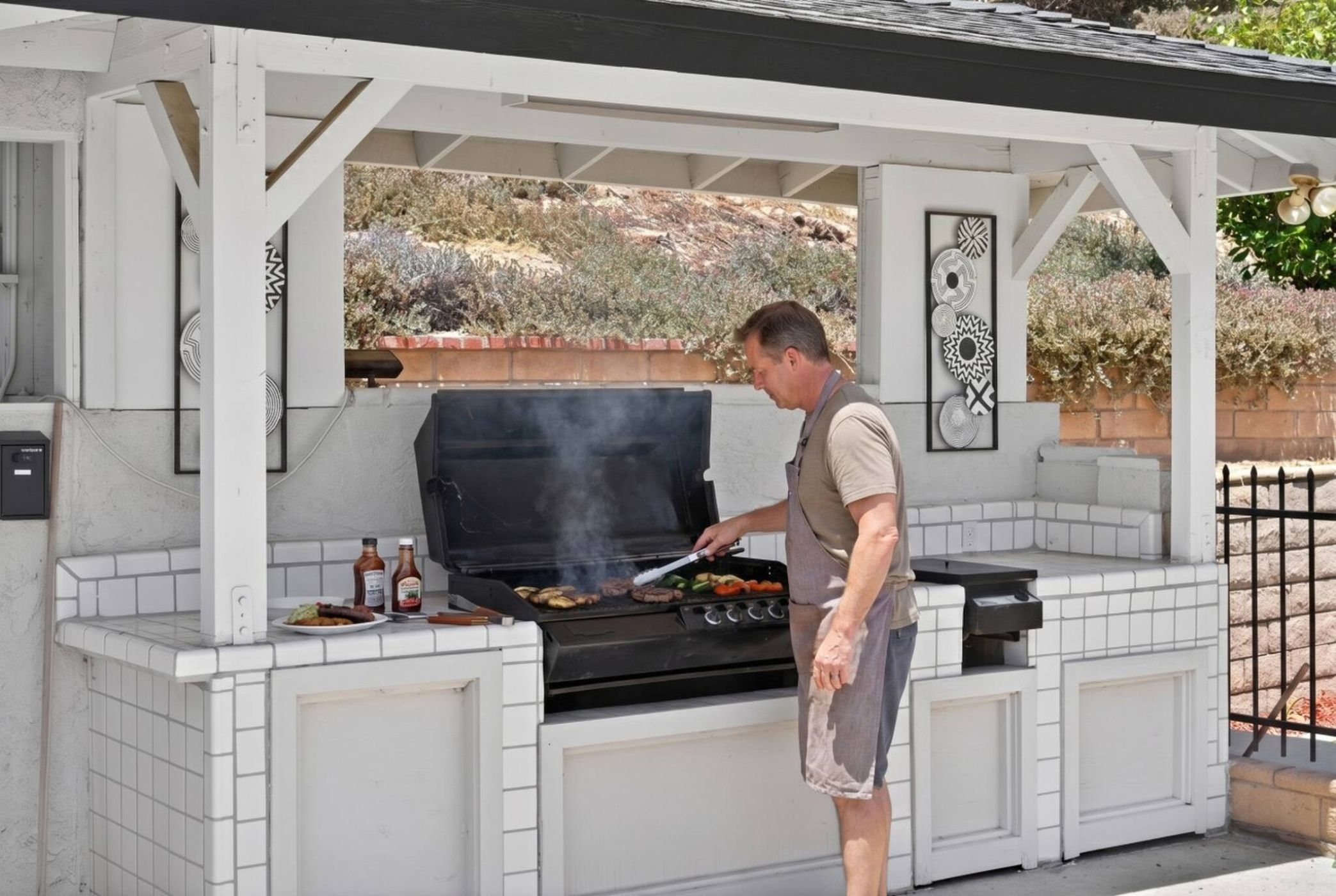 An outdoor kitchen with a grill, cooking utensils, and condiments.