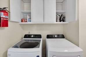 A laundry room with two front-loading washing machines, a fire extinguisher, and a cabinet above.