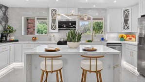A modern kitchen with white cabinetry, a central island with stools, a built-in stove, and a large window.