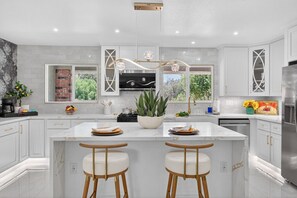 A modern kitchen with white cabinetry, a central island with stools, a built-in stove, and a large window.