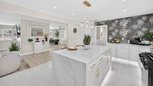 A modern kitchen with marble countertops, a central island, and a dining area with a view.