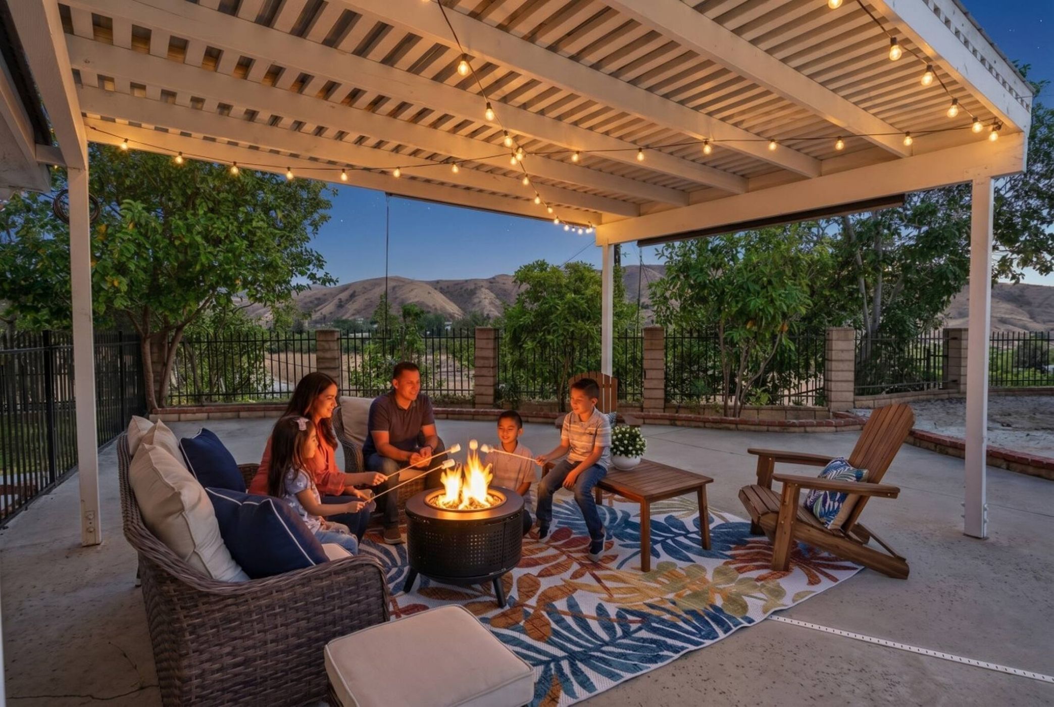 A covered outdoor seating area with a fire pit, lounge chairs, and string lights.