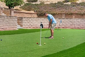 A person on a green artificial turf playing golf with a putter and a golf ball.