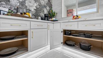 A modern kitchen with white cabinetry, a marble backsplash, and a variety of cooking utensils.