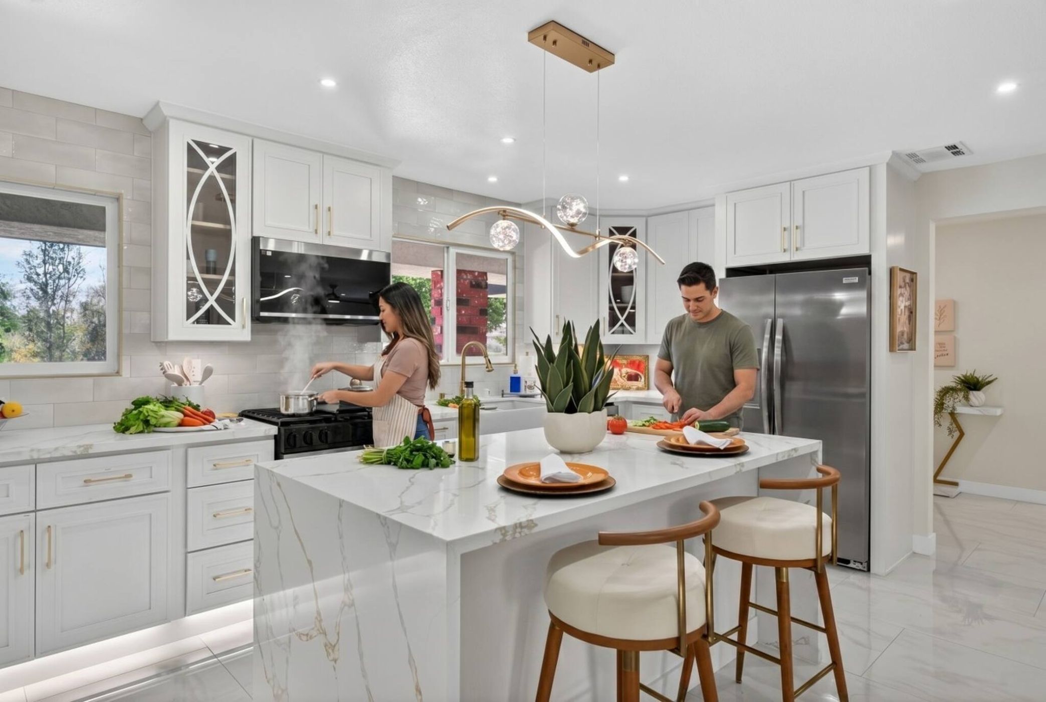 A modern kitchen with white cabinetry, a central island with stools, a stainless steel refrigerator, and a large window.