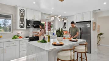 A modern kitchen with white cabinetry, a central island with stools, a stainless steel refrigerator, and a large window.