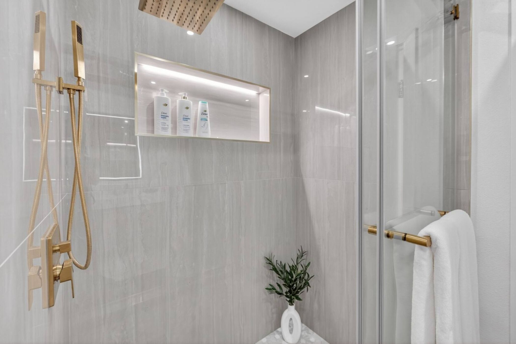 A modern bathroom with a glass shower enclosure, a white sink, and a towel rack.