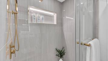 A modern bathroom with a glass shower enclosure, a white sink, and a towel rack.