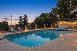 Una piscina con sillas de descanso, luces colgantes y una zona cubierta.