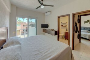 A hotel room with a bed, a television, a balcony, a bathroom, and a ceiling fan. - Beautiful Condo with pool and close to the beach, centrally located in the North Hotel Zone. (Puerto Vallarta)