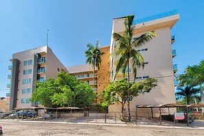 Un hotel de varios pisos con balcones, palmeras y una zona de estacionamiento techada.