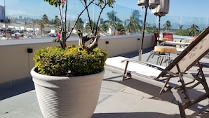 Une terrasse sur le toit, agrémentée d’un grand pot de fleurs, d’un banc en bois et d’une table avec des chaises.