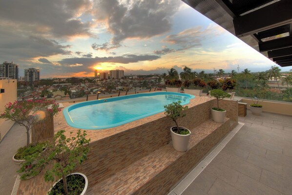 A rooftop pool with a cityscape view at sunset, surrounded by potted plants. - Beautiful Condo with pool and close to the beach, centrally located in the North Hotel Zone. (Puerto Vallarta)
