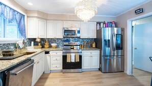 Una cocina moderna con armarios blancos, electrodomésticos de acero inoxidable, una araña y suelo de madera.